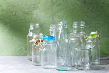 Variety of different shape empty opened glass bottles with and without lids standing on grey table...