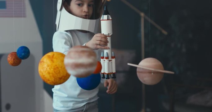 CU Little kid boy wearing cardboard astronaut helmet launching a toy rocket from a spaceport through planets. 4K UHD 60 FPS SLOW MO