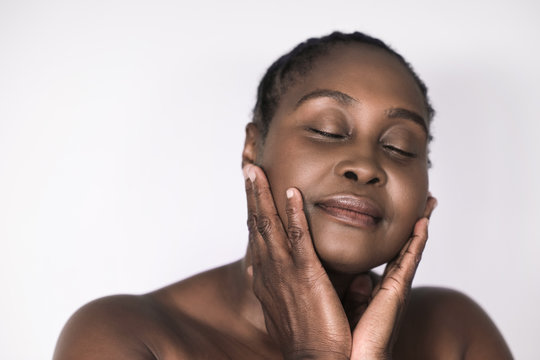 Mature African Woman Touching Her Cheeks Against A White Background