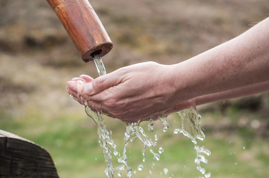 closeup of hands in the water of typical wooden fountain on moutain landscape background