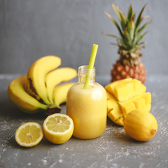 Refreshing yellow smoothie with yellow fruits on gray background