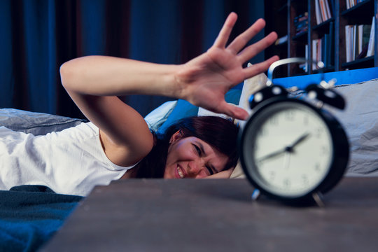 Photo of dissatisfied woman with insomnia stretching arm to alarm clock at night