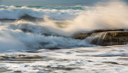 Fototapeta premium Rocky seashore with wavy ocean and wind waves crashing on the rocks