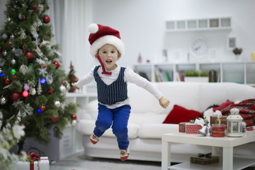 The boy is happy with the New Year. Happy child on christmas. Emotions overwhelm. A boy in a cap of Santa Claus jumps up.The New Year has come.
