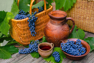 Fototapeta na wymiar Baskets and bowl with grapes. Jar and cup with wine stand on on rustic wood. Wine making background.