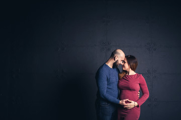 bearded man holding belly of pregnant woman in studio on dark background. Copy space.