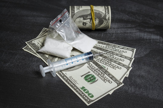 Syringe and plastic bags with drugs near a pile of dollars