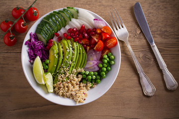 Vegetarian healthy food: quinoa, avocado, pomegranate, tomatoes, green peas, radish, red cabbage and lime salad in bowl on wooden table. overhead, horizontal