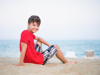 Teen boy on sand on beach - summer vacation, close-up portrait. Child looking up at camera. © valiza14