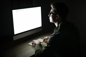 Handsome male programmer, IT person, hacker, works in computer on internet in dark room in front of pc