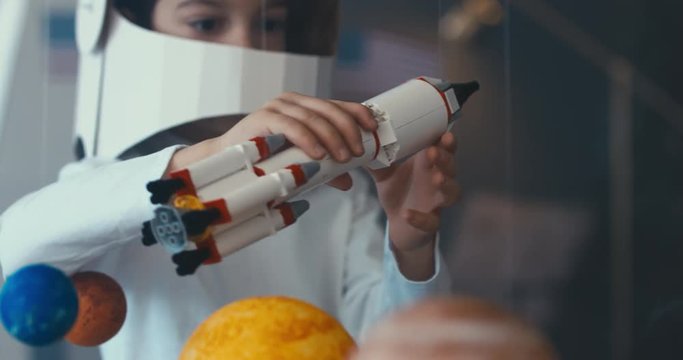 CU Cute little boy wearing cardboard astronaut helmet flying toy rocket through planets, exploring deep space. 4K UHD 60 FPS SLOW MO