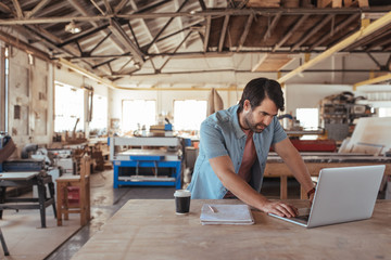 Young woodworker using a laptop in his workshop