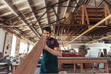 Skilled woodworker examining a wooden plank in his workshop