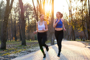 Fototapeta premium Young women run along the path in the park at sunset and laugh