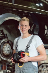 Low-angle view portrait of a confident young auto mechanic holding a new air suspension system,...