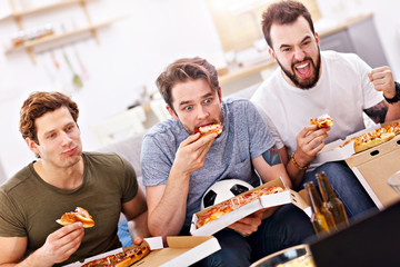 Happy male friends eating pizza and watching tv