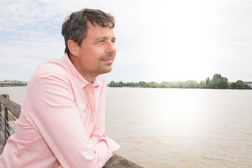 Fototapeta na wymiar Thoughtful casual man outdoors looking up Garonne river and smiling in the Bordeaux city in France