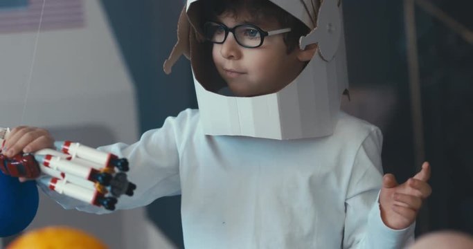 CU Cute little boy wearing cardboard astronaut helmet flying toy rocket with attached red sports roadster car to it. 4K UHD 60 FPS SLOW MO