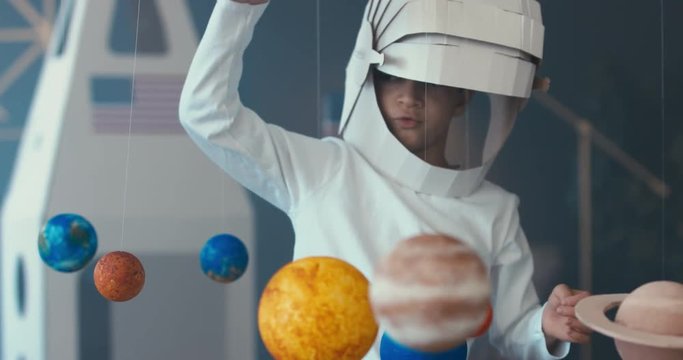 CU Cute little boy wearing cardboard astronaut helmet flying toy rocket with attached red sports roadster car to it. 4K UHD 60 FPS SLOW MO