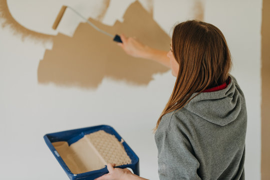 young woman painting wall with a roller and holding paint tray