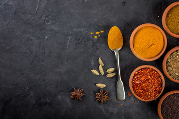 Different spices in bowls and spoon on dark background. Top view