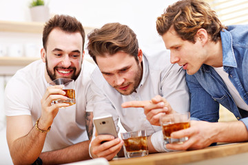 Cheerful friends having fun with smartphone and drinking at home