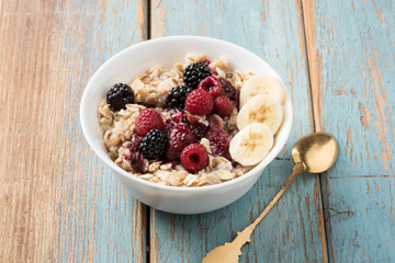 oatmeal porridge with berries and bananas in a bowl on a wooden table