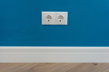European standard 220 volt wall electrical outlet on wall with baseboard and hardwood floor