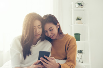 Beautiful young asian women LGBT lesbian happy couple sitting on bed hug and using phone together bedroom at home. LGBT lesbian couple together indoors concept. Spending nice time at home.