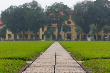 Fototapeta na wymiar Concrete pathway and grass fields alongside with a yellow building in the background at Ba Dinh Square, Hanoi, Vietnam