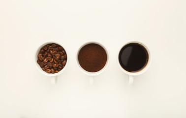 Roasted whole and ground coffee beans in cups, top view, white i