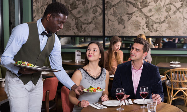 African American waiter serving couple at restaurant