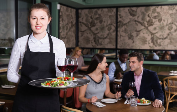 Attractive young waitress with serving tray welcoming in restaurant