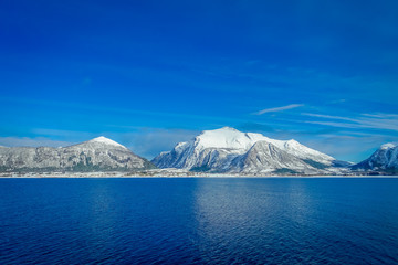 Amazing landscape of outdoor view of coastal scenes of huge mountain covered with snow on Hurtigruten voyage during a blue sky