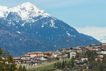 Fototapeta premium Picturesque view on the village with high mountain peaks covered in snow on the background, Dolomites, Trentino, Italy