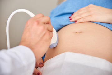 Closeup view of a pregnant womans belly while getting ultrasound scan by a male doctor.
