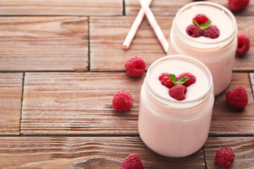 Raspberries yogurt in jars on brown wooden table