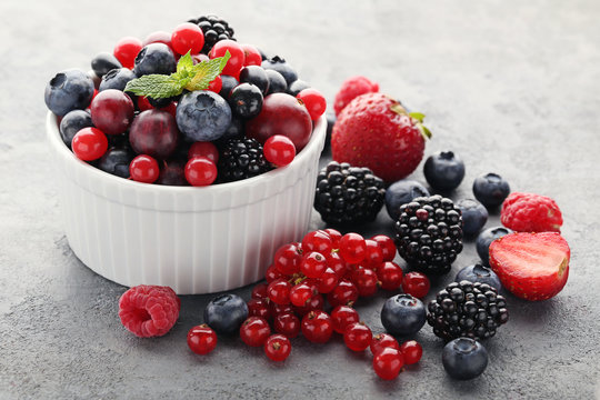 Ripe and sweet berries in bowl on grey wooden table