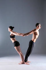 Fototapeta premium Young couple practicing acro yoga on mat in studio together. Acroyoga. Couple yoga. Partner yoga.