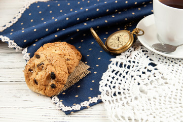 Tea cup, cookies and clock on a wooden white table working place.