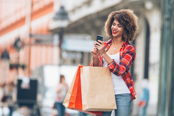 Young woman at the street with shopping bags using mobile phone 