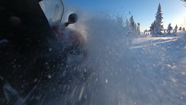 SLOW MOTION, CLOSE UP: Snowmobile takes off and sprays snow into the camera. Sled riding race in back country. Snowmobile tracks spinning, kicking up fresh snow and spraying snowflakes. Snowmobiling