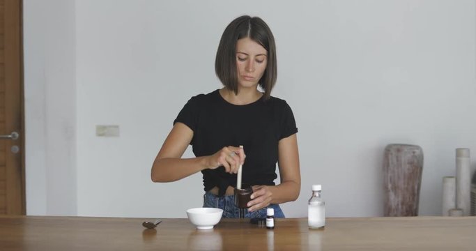 Young pretty woman makes toothbrush independently from ecological natural materials at home. Girl stirring ingredients in a jar. Zero waste concept 4k