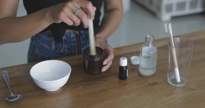 Young pretty woman makes toothbrush independently from ecological natural materials at home. Close-up of 4k footage of girl stirring ingredients in jar. Zero waste concept