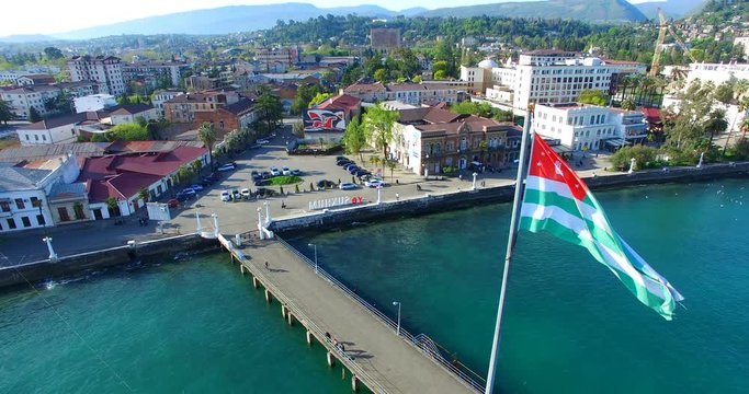 The Abkhaz flag flying over the waterfront of Sukhum on the background of blue sea and architectural sights.