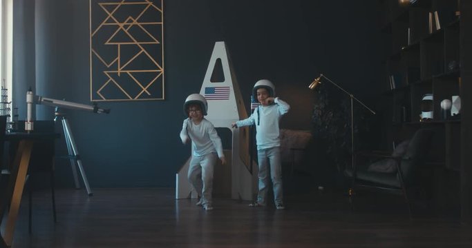 Cute little dreamer siblings brothers wearing space helmets pretending to be astronauts on Moon, getting out cardboard space rocket at home. 4K UHD 60 FPS SLOW MO