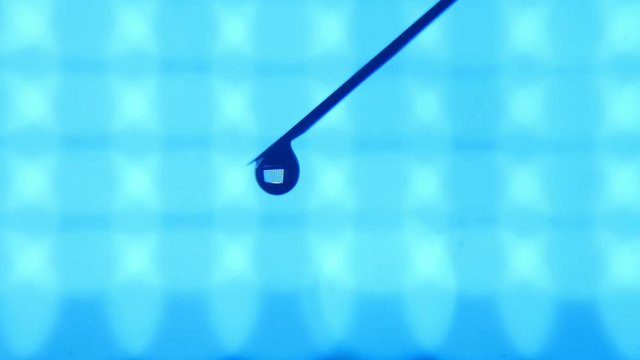 A marvelous macro of a brilliant drop of water swelling on a tip of a needle. A water stream dribbles in a turquoise laboratory.