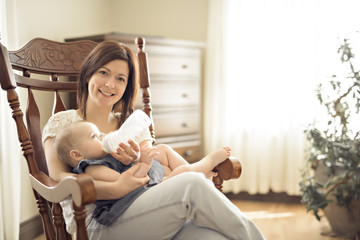 Mother holding and feed her baby child on chair