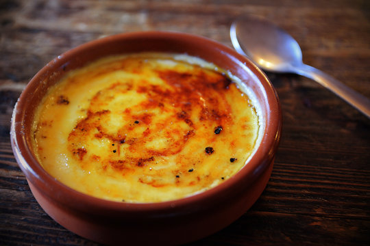 Typical "crema catalana" served on a clay plate on a rustic wooden table with a spoon. Empty copy space for Editor's text.