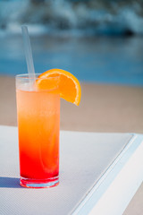 Glasses with colored cocktails on the beach with blue water in the background